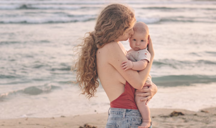 mum holding baby on beach when travelling with a new baby